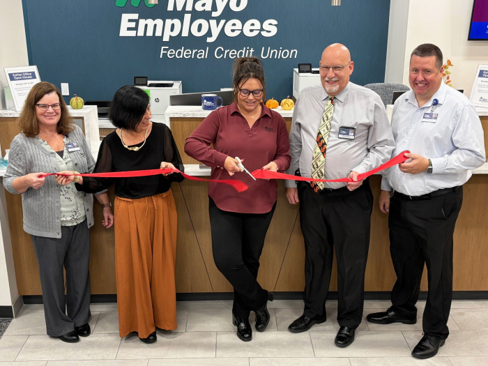 A group of five people stand in front of MEFCU sign, proudly cutting a ribbon to signify the opening of the newest office location