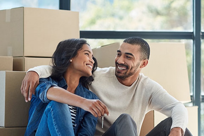 couple sitting on floor in front of moving boxes, mans arm around womans shoulder